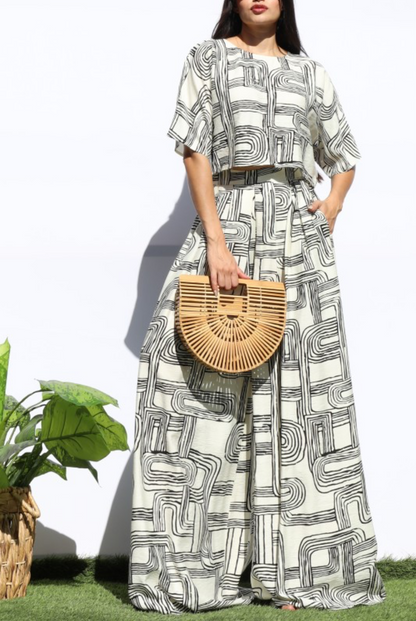 A woman modeling a matching two-piece set featuring a black and white geometric maze-like pattern, holding a round woven straw handbag.